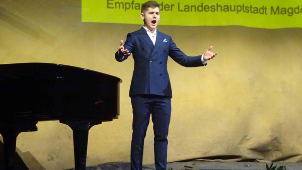 Ein Mann auf einer Bühne singt, daneben ein Klavier