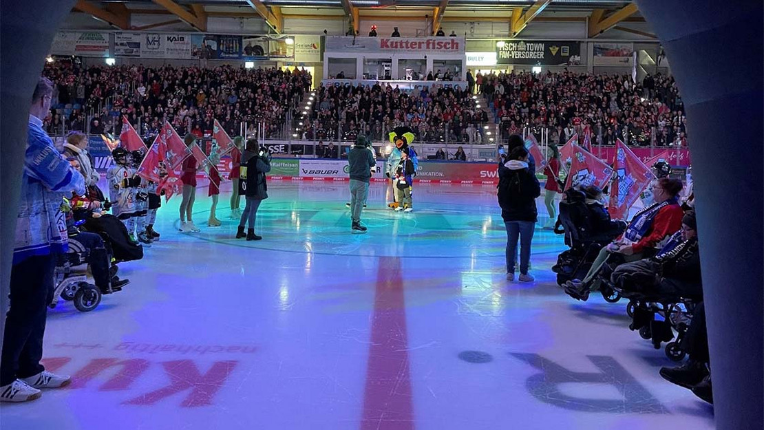 Mehrere Personen in Rollstühlen sind vor einem Eishockeyspiel auf der Eisfläche. 