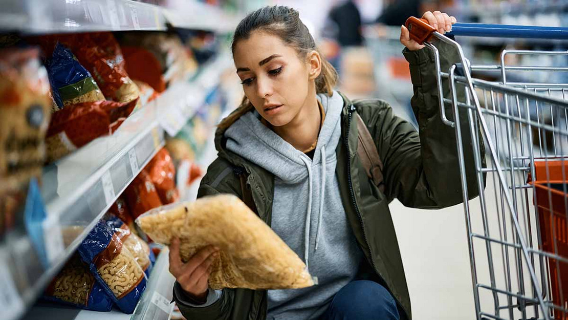 Frau im Supermarkt betrachtet eine Nudelpackung