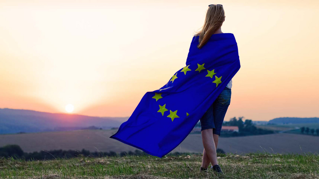 Frau mit EU-Flagge steht auf einem Feld. 
