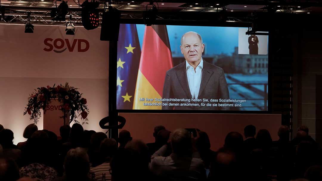 Olaf Scholz spricht auf einer Videoleinwand. 