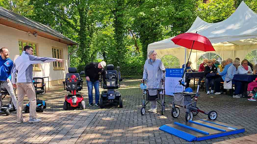 Hof mit Menschen, die Rollatoren und Elektro-Rollstühle testen.