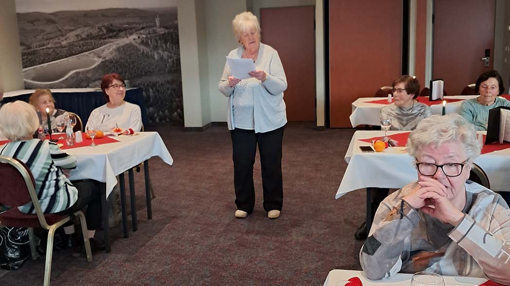 Frau steht zwischen Tischen mit Zuhörer*innen