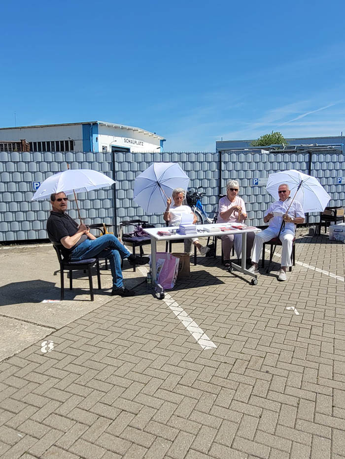Vier SoVD-Mitglieder sitzen mit Sonnenschirmen am Infostand